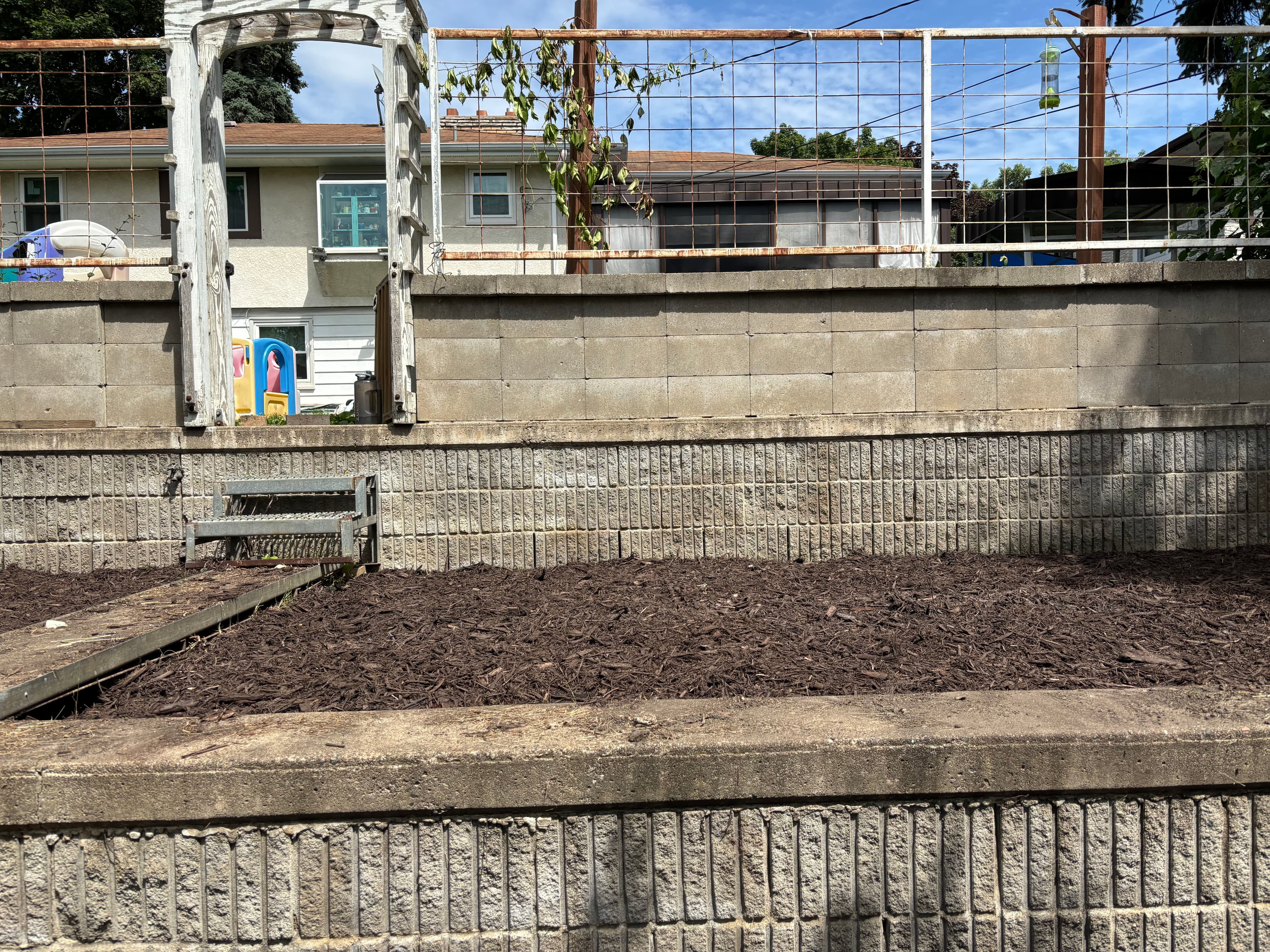 Garden area with mulch and stone borders, featuring an archway and fencing in a residential setting.