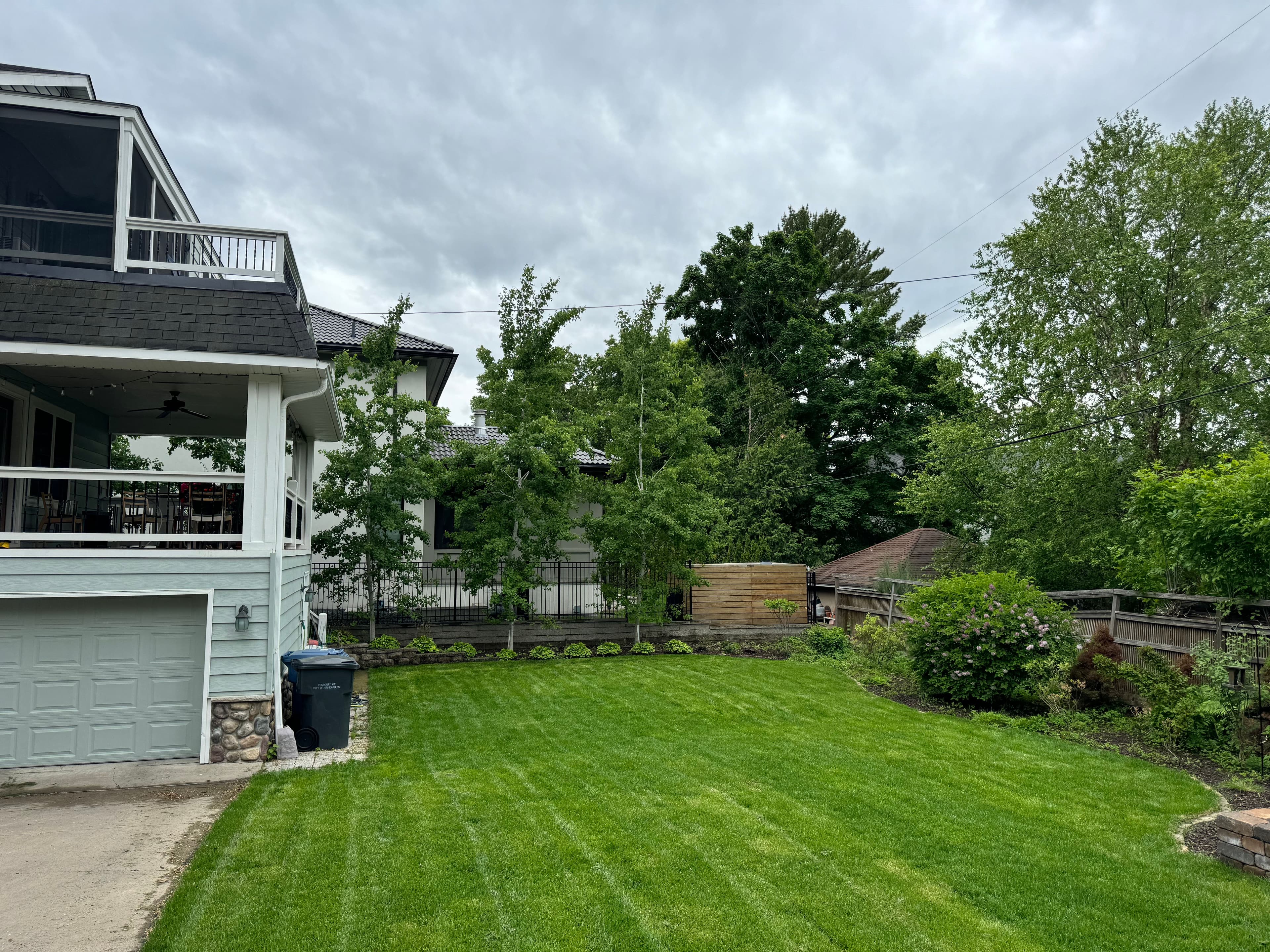 Lush green lawn with landscaped garden, modern house, and cloudy sky in residential area.